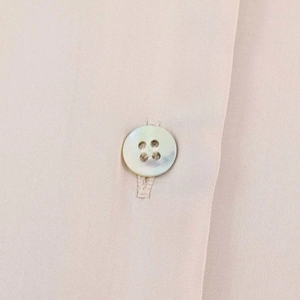 Macro shot of pearl luster button on pale pink satin blouse with fine fabric texture