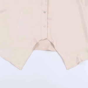 Detailed macro view of the asymmetric sharp hemline and buttons on the beige satin shirt