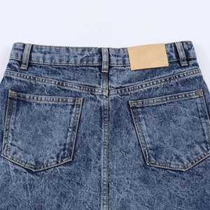 Close-up of high-waist denim skirt back pockets and brown leather patch in acid wash finish