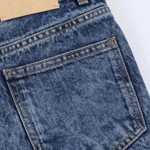 Detail of blue wash denim skirt back pocket with yellow stitching and leather waist patch