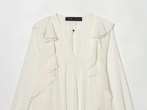 Detailed view of white ruffled shirt featuring vertical pleats and a keyhole neckline button