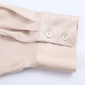 Close-up of champagne satin blouse sleeve featuring pleated details and double button cuffs