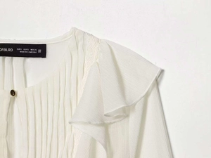 Detail of ruffled collar and gold button on white long sleeve blouse with brand label