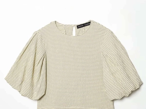 Detail of light beige checkered fabric texture and puff sleeve stitching on the blouse