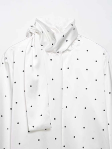 Détail du col à nœud élégant et du motif à pois argentés sur le chemisier de femme