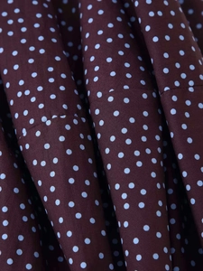 Détail de tissu à pois rouge-brun avec plis verticaux sur une chemise à manches
