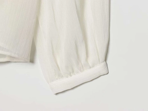 Detail of white ruffled long sleeve cuff showing semi-transparent pleated chiffon texture