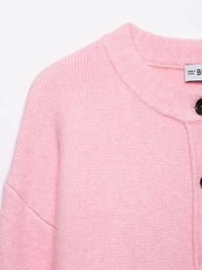 Detail of pink knit cardigan showing round neck and textured fabric with buttons