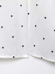 Détail de tissu blanc à pois argentés montrant les finitions précises de l'ourlet