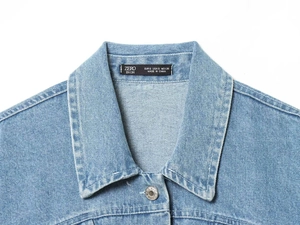 Detail view of denim jacket collar showing metal button and brand label on light blue fabric