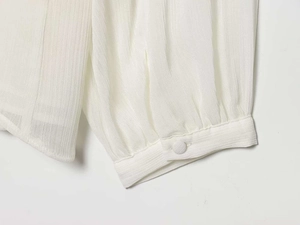 Macro shot of vertical plissé pleats and fabric-covered button on white blouse cuff