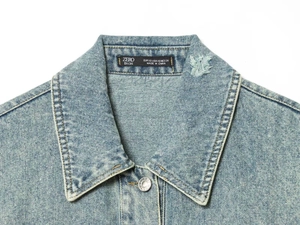 Dettaglio del colletto e dell'etichetta di una giacca di jeans blu chiaro con strappi