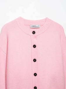Close-up of pink knit cardigan showing round neck and black buttons on textured wool fabric