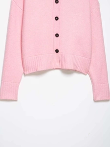 Close-up of pink knit cardigan showing fine texture, black buttons and ribbed hem details