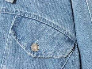 Detailed macro view of light blue denim fabric texture and silver metal button on jacket