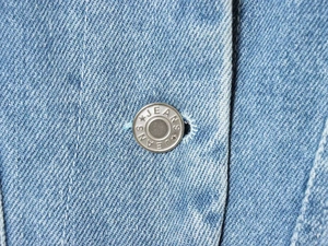Macro detail of silver JEANS button on light blue wash denim jacket fabric