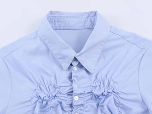 Detail shot of light blue stretch poplin shirt featuring front pleats and white buttons