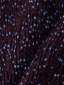 Détail du tissu smocké à pois bleus sur une texture bordeaux profonde