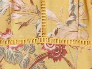 Dettaglio dell'abito giallo a fiori con stampa vintage e inserti in pizzo a scala