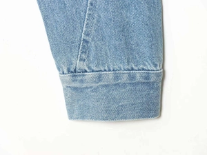Detailed close-up of light blue denim jacket cuff showing precise stitching and fabric texture