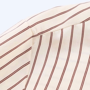 Detalle de la costura del hombro y tejido de sarga de rayas rojas en camisa beige