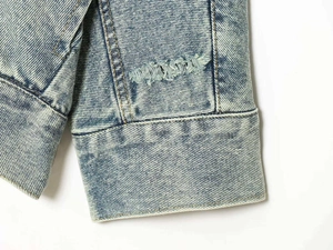 Macro dei polsini di una giacca di denim blu con lavaggio pesante e dettagli strappati