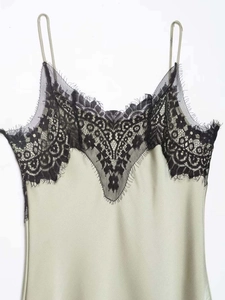 Detail of delicate black lace trim on the V-neckline of a green satin slip dress