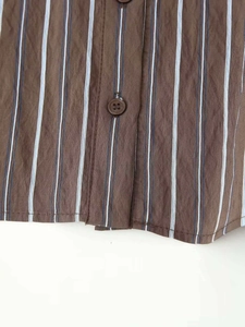 Détail d'une chemise rayée marron montrant les boutons de la patte et la texture du tissu