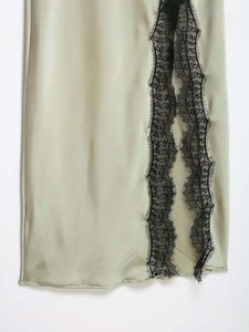 Detail shot of light sage green satin fabric with delicate black eyelash lace trim