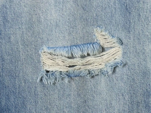 Nahaufnahme von hellblauem Denim-Stoff mit Rissen und sichtbaren weißen Baumwollfasern