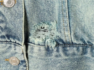 Dettaglio della giacca di jeans lavaggio chiaro con bottone metallico e bordi sfrangiati
