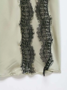 Detailed macro view of black eyelash lace trim on a light sage green satin slip dress