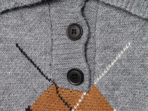 Detail der grauen Strickjacke mit braunem Rautenmuster und schwarzen Rundknöpfen