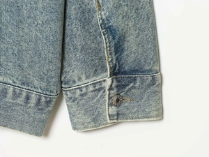 Dettaglio del polsino in denim azzurro con bottone in metallo e cuciture dorate a contrasto