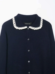 Detail of navy knit cardigan featuring white crochet lace collar and button closure