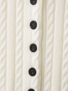 Detailansicht der cremefarbenen Strickjacke mit Zopfmuster und verzierten schwarzen Knöpfen