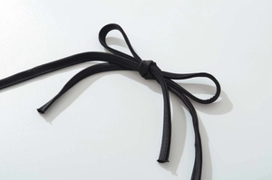 Dettaglio di una spallina in raso nero annodata con un fiocco su un top bianco chic