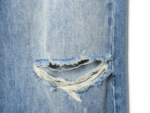 Macro detail of vintage light blue denim jeans featuring distressed ripped frayed edges
