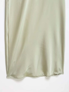 Detailed close-up of light green satin dress hem showing smooth fabric and stitching