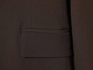 Detail of a dark brown suit jacket featuring a classic flap pocket and twill texture fabric