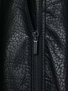 Détail de la veste en similicuir noir grainé avec fermeture éclair gris fusil en gros plan