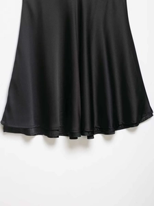 Close-up of black satin dress with elegant draped hemline and smooth glossy texture