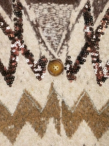 Detail of geometric jacquard knitwear with sequin embroidery and an amber resin button