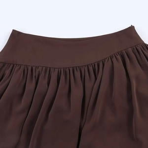 Detailed macro view of the smooth pleated high waist and silk satin fabric of the brown skirt