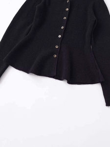 Detail of black knit cardigan featuring a peplum hem and contrasting textured buttons