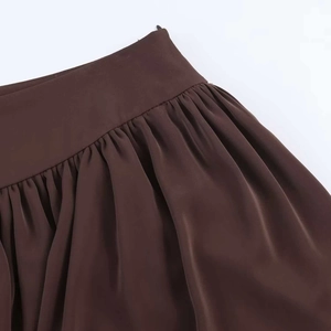 Detail shot of high waist dark brown skirt featuring pleated waistline and satin fabric texture