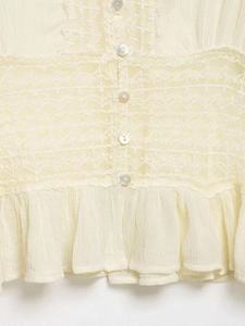 Detail of cream chiffon blouse featuring delicate lace stitching and pearl buttons