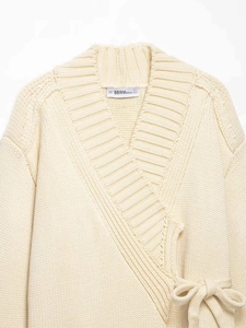 Close-up of cream wrap knit cardigan featuring wide ribbed V-neck and branded inner neck label