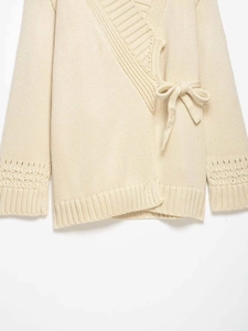Detail of cream wrap cardigan featuring cross-over tie waist and crochet hollow sleeves