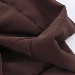 Detailed macro shot showing fabric texture, pleats, and stitching of the high-waisted brown skirt